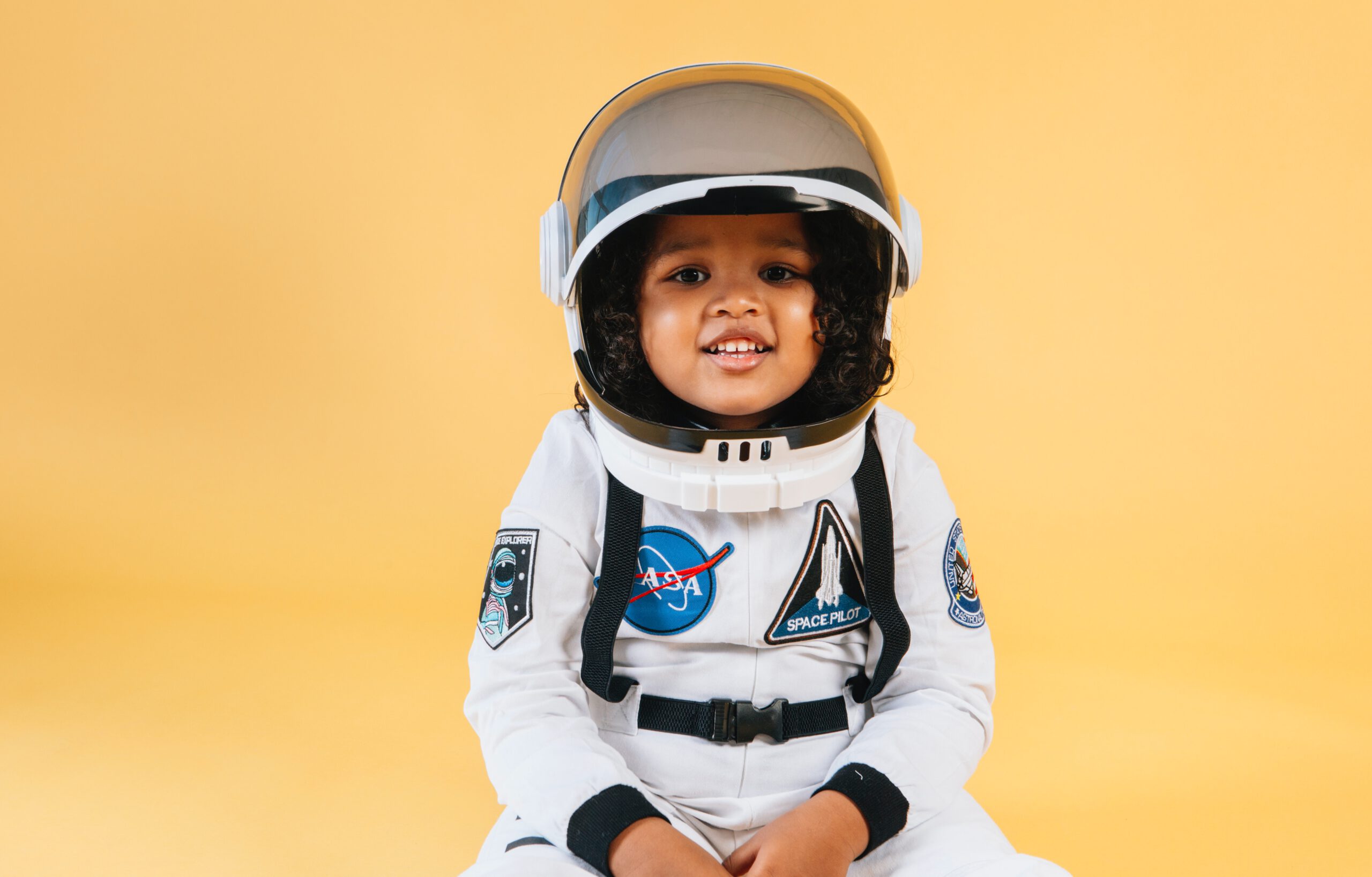 Uśmiechnięty mały chłopczyk w pełnym stroju astronauty na żółtym tle